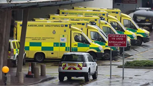 Five Ambulances Are Lined Up Outside A Hospital. Cars With Emergency Yellow And Red Zigzags Are Also Visible. A Sign Says Ambiwans Yn Unig Ambulance Only